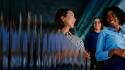 Three professional women smiling with data visualization background in modern office setting.