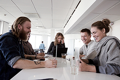 A group of people laughing and smiling over a laptop at the table