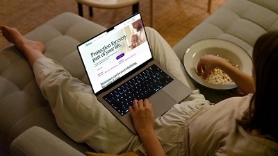 A person on a couch, browsing an insurance website on a laptop. They are eating popcorn from a bowl.