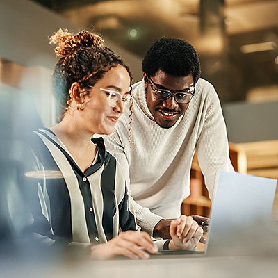 Two professionals smiling while reviewing content on a laptop in a modern office.