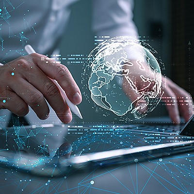 A person uses a stylus on a digital tablet, visualizing a glowing digital globe with interconnected lines and data, signifying technology and innovation.