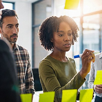 Team collaborating in a modern office, woman in green shirt presenting ideas on yellow sticky notes.