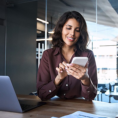 Woman at office desk smiling while using smartphone.