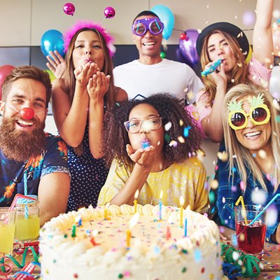 Friends celebrating a birthday with balloons, confetti, cake, and drinks.