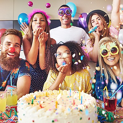 Friends celebrating a birthday with balloons, confetti, cake, and drinks.