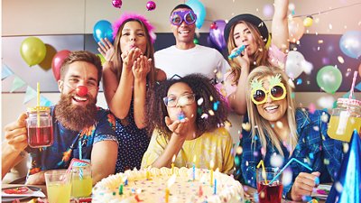 Friends celebrating a birthday with balloons, confetti, cake, and drinks.