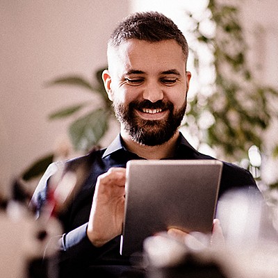 Smiling person with a beard using a tablet, with a blurred background.