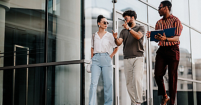 Three people walking outside a modern glass building, one holding a blue folder.