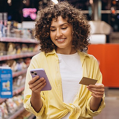 Woman holding smartphone and loyalty card at retail store checkout.