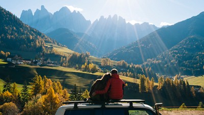 A couple sitting on top of a vehicle looking at a beautiful valley and mountains