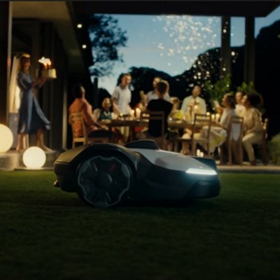 Robotic Husqvarna lawn mower on a grassy slope with red-accented wheels and headlights.