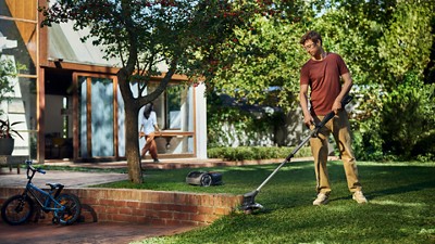 Person trimming grass in a backyard with a tree, bicycle, and Husqvarna mower nearby.