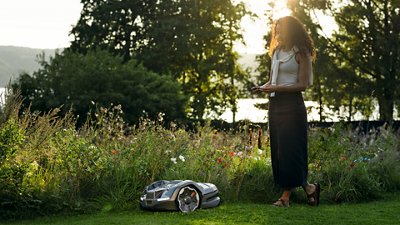 Robotic Husqvarna lawn mower on a grassy slope with red-accented wheels and headlights.