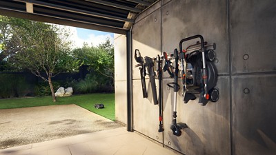 Garden tools hanging in a garage with a Husqvarna mower visible on the lawn outside.