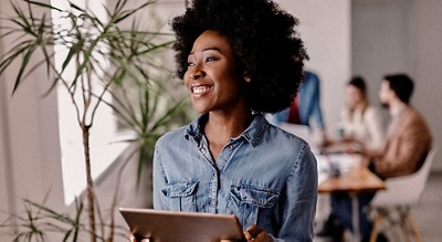 A smiling woman in the office holding a tablet in her hands.