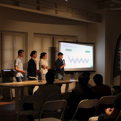 Four people standing, giving a presentation with a projector showing a graph chart