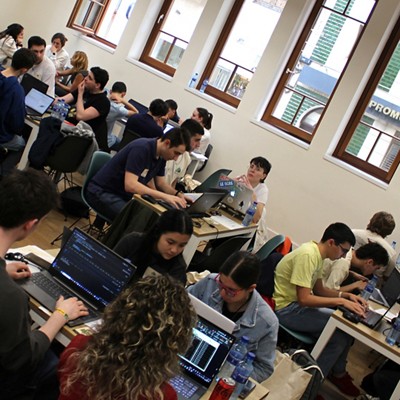 A large collection of students sitting at tables in groups working on computers