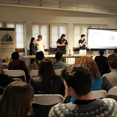 Four people standing, giving a presentation with a projector showing a graph chart in front of an audience