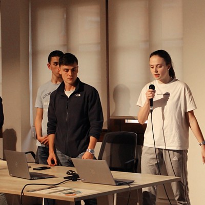 two men and a woman with a ponytail standing conducting a presentation