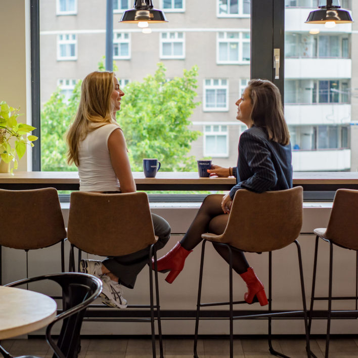 Two of our colleagues sitting by the window, talking with Merkle cups