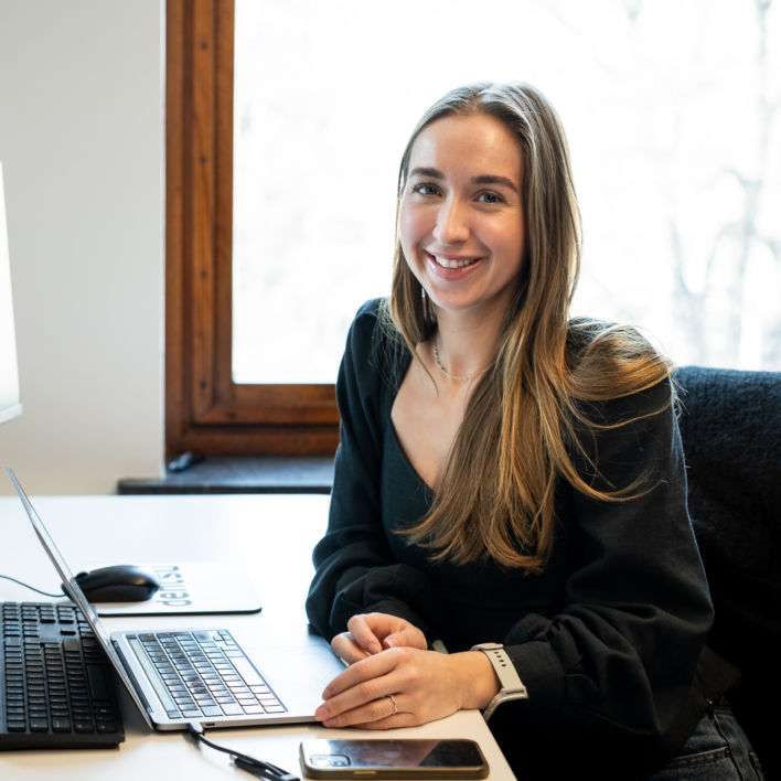 A colleague smiling towards the camera while working from their laptop