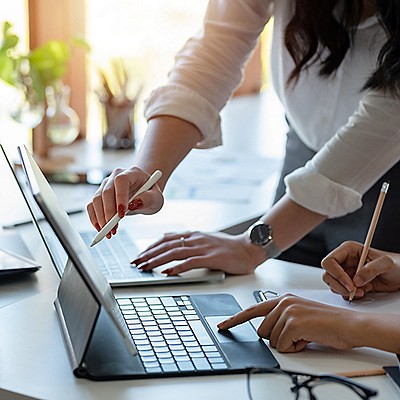 Two people collaborate at a desk, using a tablet and digital pen. One points at the screen, while the other takes notes. 