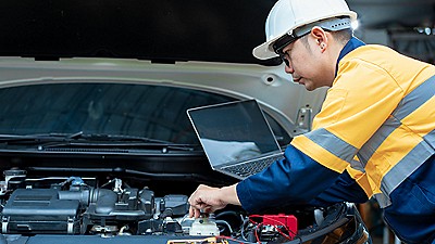 man looking under the hood of a car with a laptop