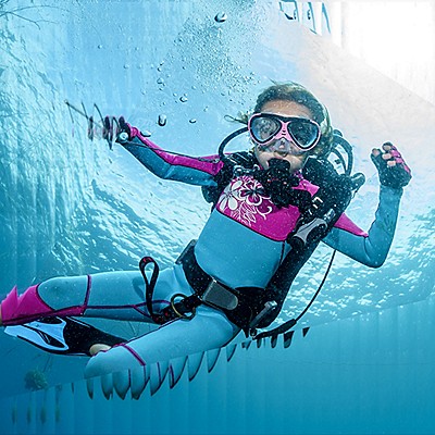 Scuba diver smiling underwater in pink and blue diving gear.