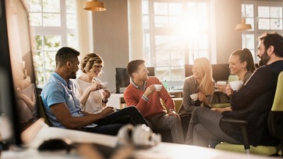 A group of six people socialize in a bright, modern office, enjoying drinks and engaging in conversation amidst a warm atmosphere.