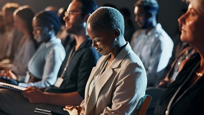 A diverse group of people sits attentively in a dimly lit conference room. 