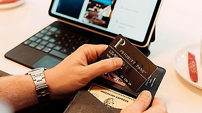A person holds a black Priority Pass card above an open wallet
