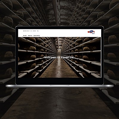Laptop screen showing Emmi UK homepage with cheese wheels and the text ‘Welcome to Emmi UK.