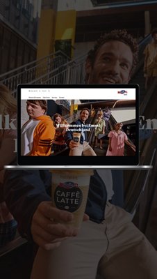 Emmi Germany website on a laptop screen with a banner showing people holding Emmi Caffè Latte and the text ‘Welcome to Emmi Germany.