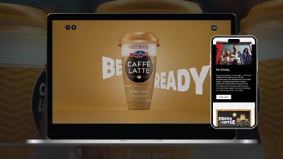 Laptop and smartphone display an Emmi CAFFÈ LATTE Macchiato ad with the slogan ‘Be Ready’.
