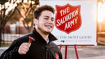 A young man ringing a bell in front of a Salvation Army bucket