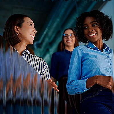 Three professional women smiling with data visualization background in modern office setting.