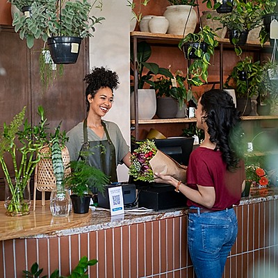 A florist in an apron smile warmly at a customer handing over a bouquet.