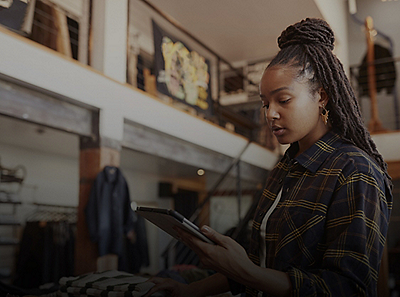 A young woman stands in a modern retail store holding a digital tablet.