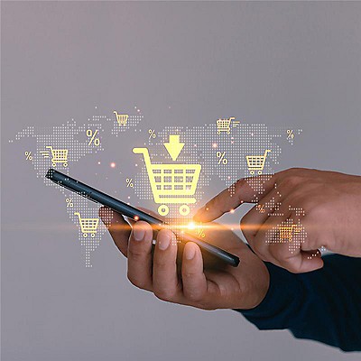 A person uses a smartphone with a glowing shopping cart icon above it. Digital symbols of carts and percentages overlay a subtle world map, suggesting online shopping.
