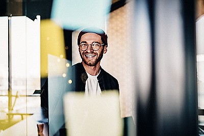 Cheerful caucasian hipster guy in trendy eyewear satisfied with creative job laughing sitting near stickers with ideas in office, 20s smiling carefree male student enjoying learning in business school