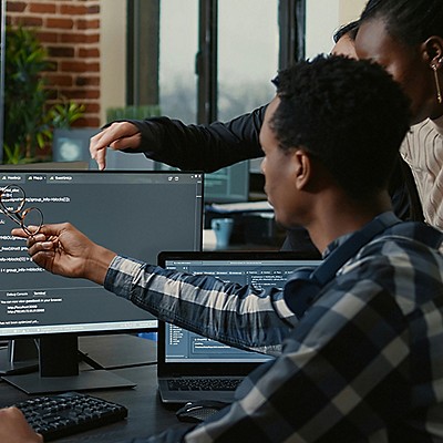 Two colleagues review and discuss a piece of code displayed on their system