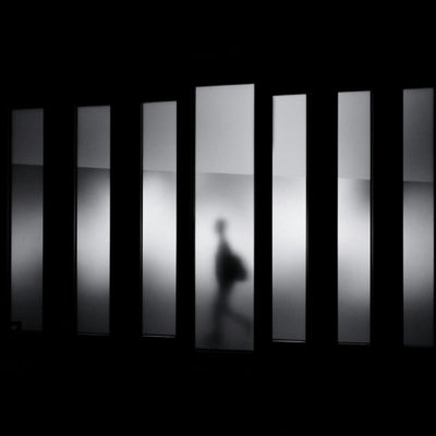 A person walks in a dark space, their form highlighted by a bright light shining from behind them.