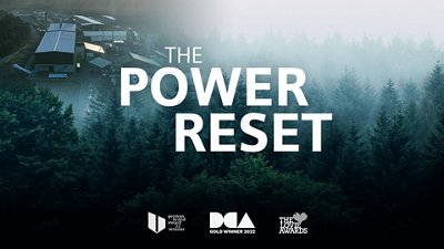 Luftaufnahme eines Waldgebiets mit einem Industriekomplex, auf dem in großen weißen Buchstaben der Text „THE POWER RESET“ zu sehen ist.
