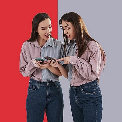 Two young women are focused on their phones, sharing a moment of engagement and conversation.