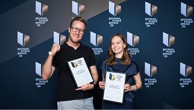 Two award winners holding German Brand Award 2026 certificates in front of the event backdrop.