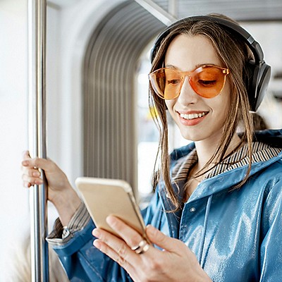 A woman wearing sunglasses and headphones relaxes on a train, immersed in her music during the commute